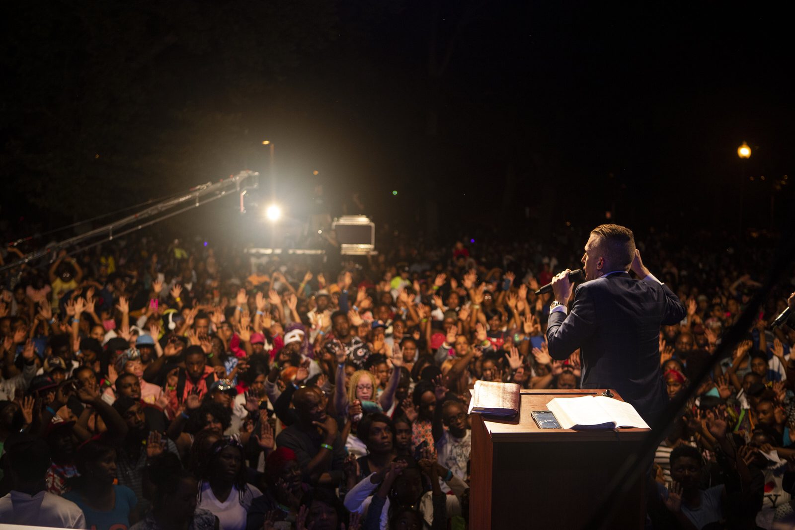 An evangelist preaching to a large crowd at a nighttime crusade