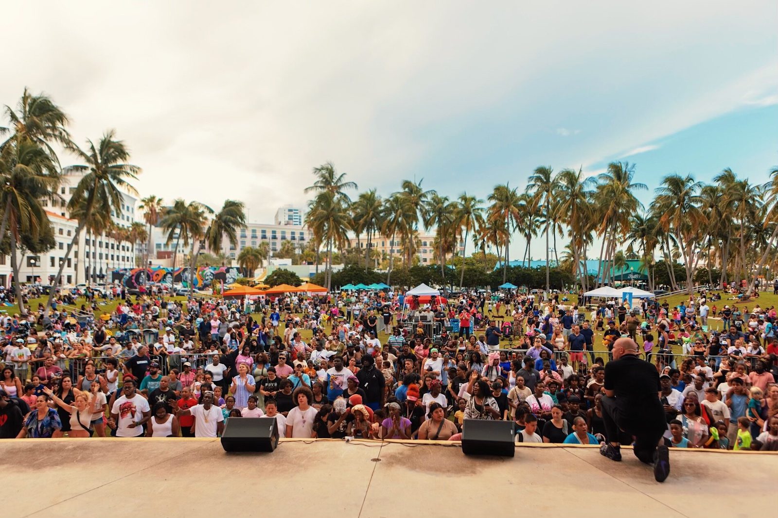 A large crowd under palm trees at an outdoor evangelistic crusade