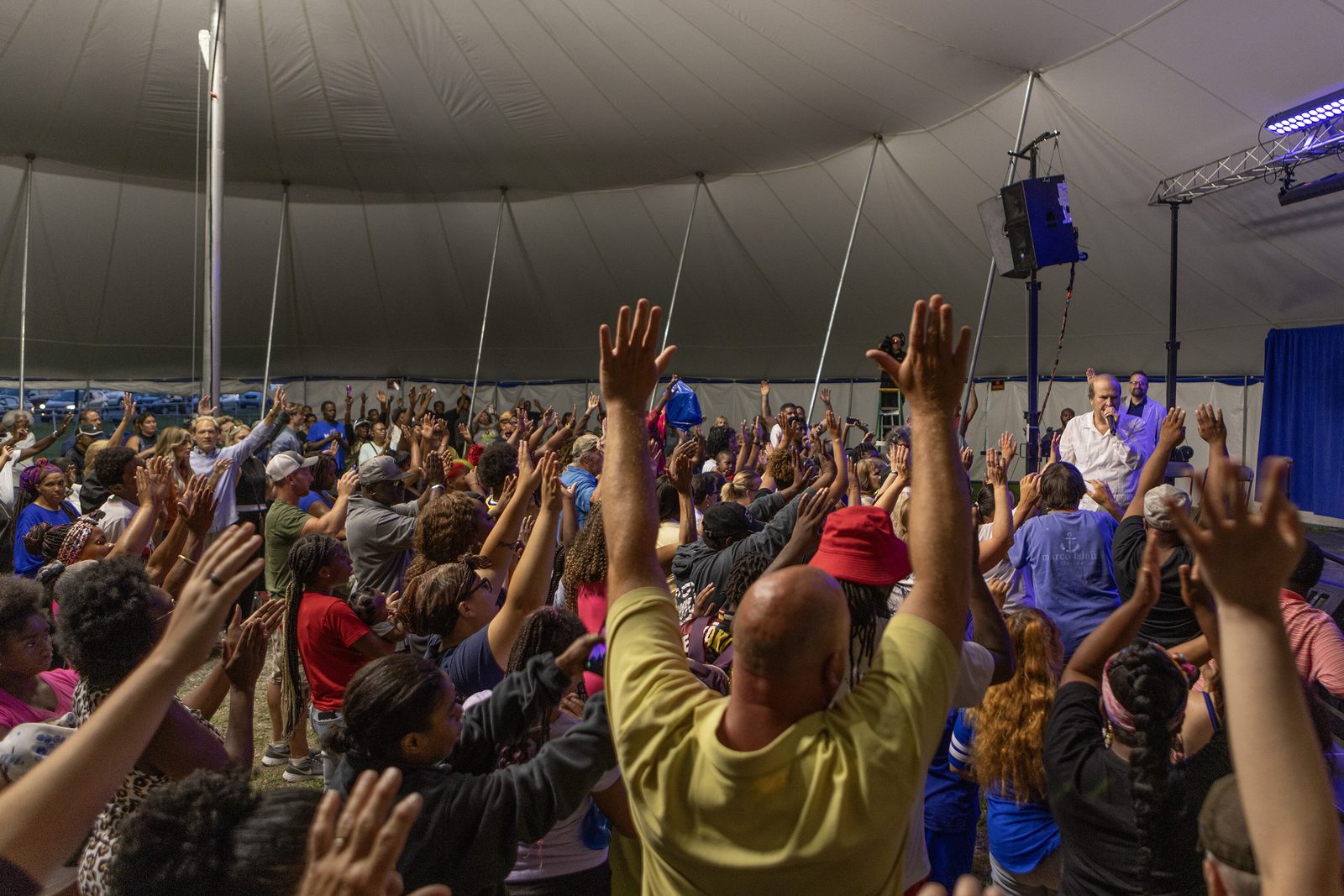 Hands raised in worship under the tent at a tent revival meeting